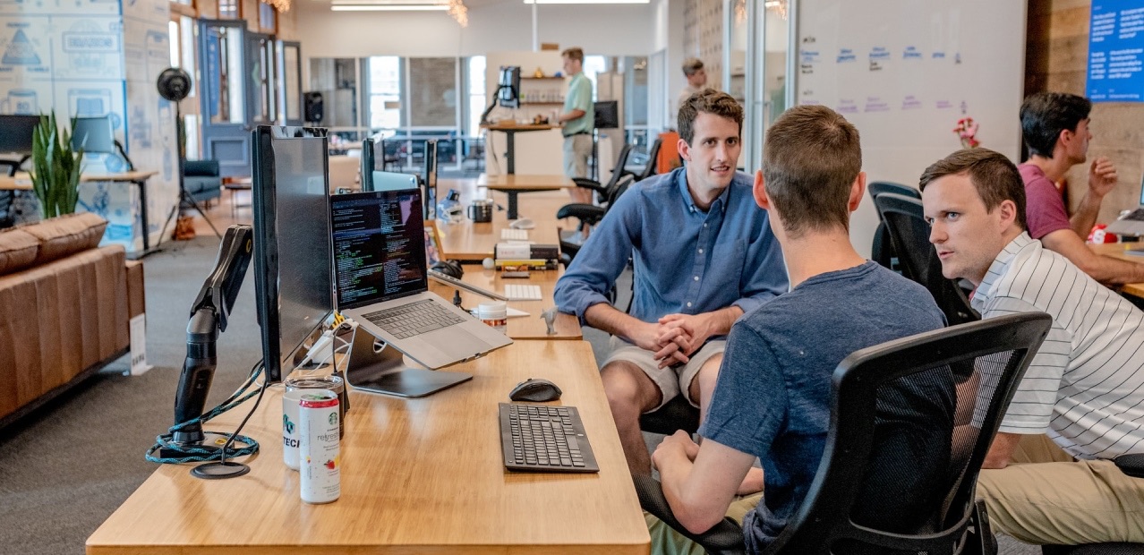 Drie collega's in gesprek aan een werkplek in een open kantoor.