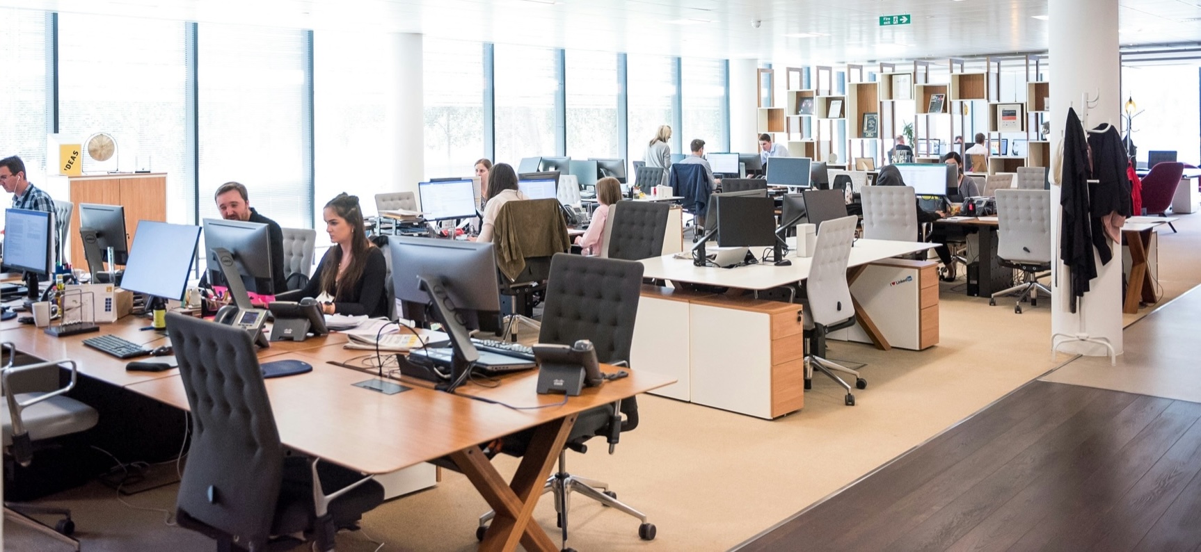 Een open kantoortuin met medewerkers achter bureaus met beeldschermen en telefoons.