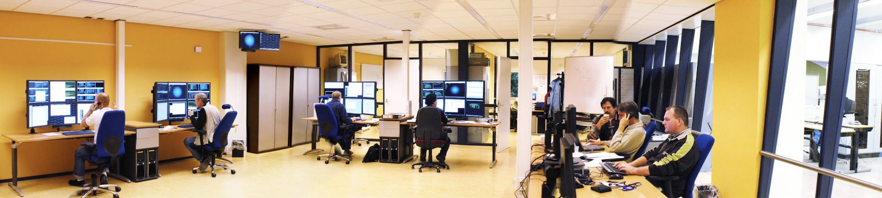 De operationsvloer van het datacenter: operators achter werkplekken met meerdere schermen vol monitoringoverzichten.