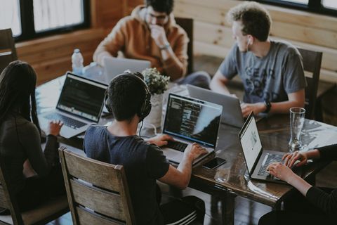 A team of developers working together on laptops at a wooden table.